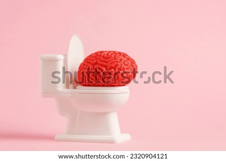 Model of human brain sitting on the white toilet on pastel pink color background. Brainwashing concept minimal art poster.