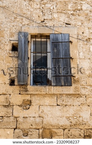 Vertical photography of old window with broken wooden shutters on an old cracked stone wall.	