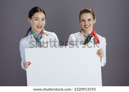 happy elegant air hostess women in blue skirt, white shirt and scarf with blank billboard against grey background.