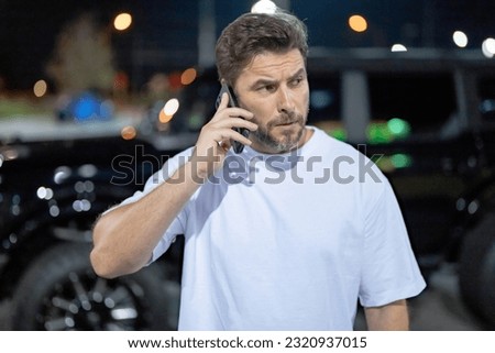 Angry man talking on phone outdoor. Angry hipster talking on phone near car on night city street. Serious angry guy talking on phone. Pensive handsome hipster look angry, talking on phone. Royalty-Free Stock Photo #2320937015
