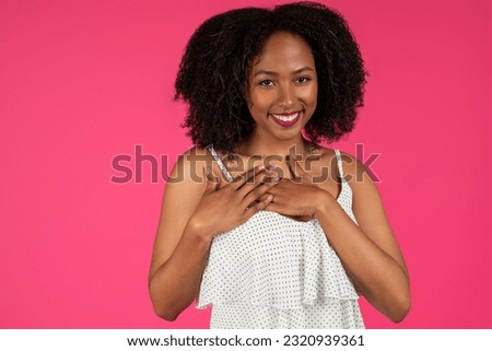 Glad young black curly lady presses hands to chest, makes sign of gratitude, thank you, isolated on pink background, studio. Love gesture, emotions, lifestyle, ad and offer