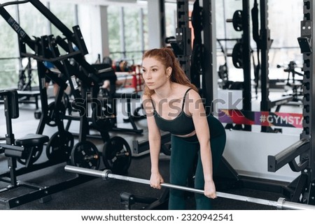 young athletic caucasian woman trains in fitness gym, deadlift with barbell, redhead girl in green top and leggings, healthy lifestyle concept