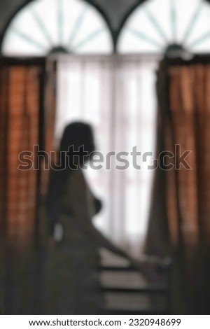 blurry photo of woman looking outdoors from behind bedroom window.
