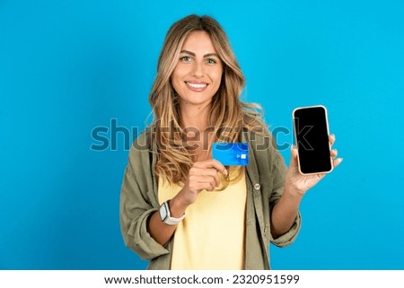 Photo of adorable young beautiful blonde woman wearing overshirt holding credit card and Smartphone. Reserved for online purchases