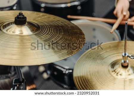 close-up view of snare drum and hands with wooden drumsticks, young caucasian woman playing black drum set with golden cymbals, sitting in rehearsal room for rock bands, rhythmic music concept Royalty-Free Stock Photo #2320952031