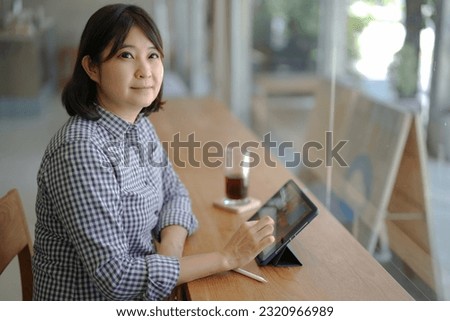 Asian woman using digital tablet and smart pen on wooden table for working business, sharing information.