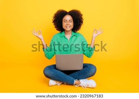 Meditation, tranquility. Full length photo of calm relaxed african american or brazilian woman, sits on isolated yellow background with a laptop, meditate with eyes closed, take care of mental health
