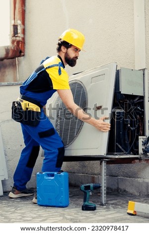 Licensed expert starting work on out of order air conditioner, using power tool to dismantle condenser metal coil panel. Skilled wireman opening hvac system to check for bad wiring Royalty-Free Stock Photo #2320978417