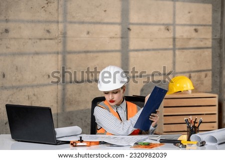 engineer in helmet and vest civil worker smart young cute blonde girl writing plan