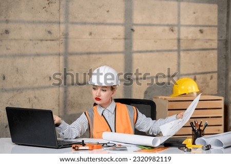 engineer young smart cute blonde girl civil worker in helmet and vest on computer