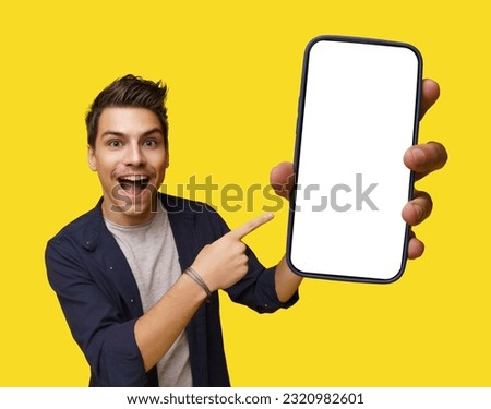 Smiling young and handsome man holding mobile phone with white screen, offering ample copy space. Image is isolated on clean white background, creating versatile canvas for various design needs. High Royalty-Free Stock Photo #2320982601