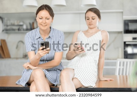Joyful mother with adult daughter write messages in instant messengers on smartphones at home Royalty-Free Stock Photo #2320984599
