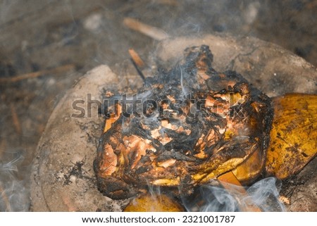 Photo of traditional Indonesian food, a rooster being grilled with billowing smoke