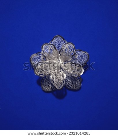 Filigree silver brooch with floral pattern on blue background.