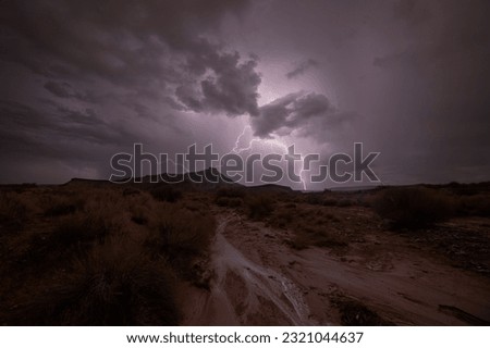 A bolt of lightning zags across the sky making the clouds glow and lighting the ground where water from the rain runs down a sandy wash in the desert of Southern Utah below Gooseberry Mesa.