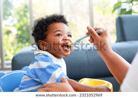 Happy smiling boy with mom while eating in the living room at home. Preschool child development, food menu for 1 year olds Royalty-Free Stock Photo #2321052969