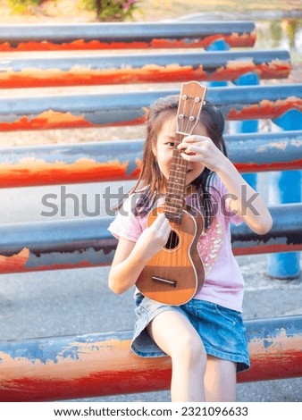 Little asian child girl play the ukulele, in the garden on the Steel pipe, practice to play