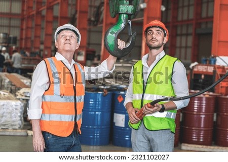 senior male factory owner and male worker wearing safety helmets look at a crane lifting loads in a warehouse inspecting its operation. Royalty-Free Stock Photo #2321102027