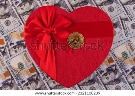 Gold coin with bitcoin cryptocurrency symbol and a gift box in the form of a human heart symbol against the background of 100 US dollars bills