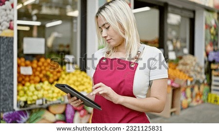 Young beautiful hispanic woman wearing apron using touchpad at fruit store