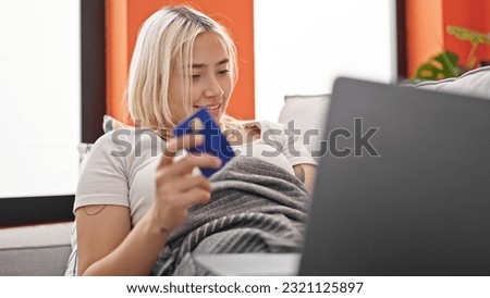 Young beautiful hispanic woman shopping with laptop and credit card lying on sofa at home