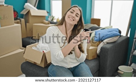 Young beautiful hispanic woman using smartphone sitting on sofa at new home