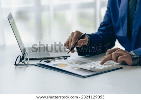 Businessman holding pen pointing to market graph and working on laptop computer working using calculator for mathematics on wooden table at office finance concept close up pictures