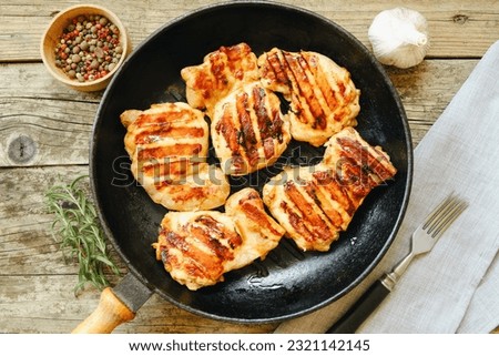 View from above. Grilled chicken thigh fillet with strips on a rustic wooden table in a cast iron pan, with rosemary, garlic pepper and fork. Flat lay. Royalty-Free Stock Photo #2321142145
