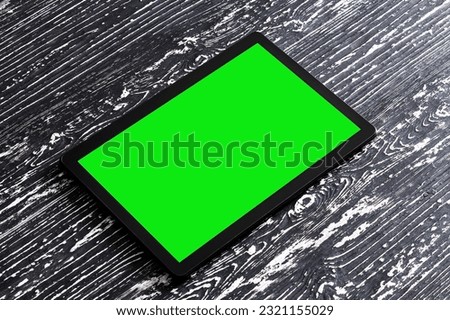Black tablet with green screen on a wooden table mock up. Copy space chroma key display. Blank for design.