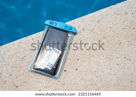 Waterproof case with money and a smartphone on the background of the pool on a sunny summer day.