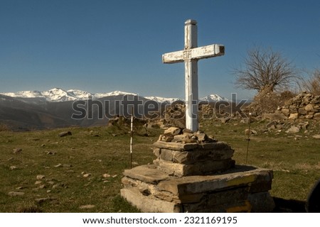 White wooden cross on a stone pedestal on the Camino de Santiago, in the background snowy mountains.