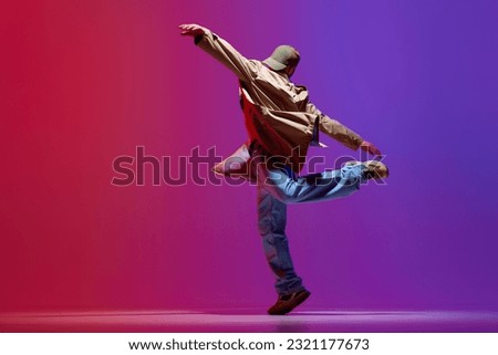 Dynamic image of young talented guy in stylish clothes dancing contemp, hip-hop against pink purple studio background. Concept of art, street style dance, fashion, youth, hobby, dynamics, ad Royalty-Free Stock Photo #2321177673