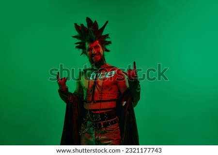 Expressive young man, rock musician, punk with neon filter on body posing against green studio background in neon light. Concept of music, lifestyle, subculture, art, youth, human emotions