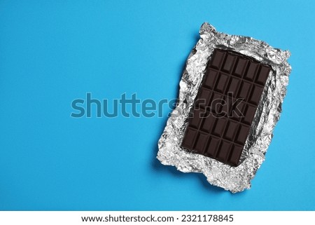 Delicious dark chocolate bar with foil on light blue background, top view. Space for text Royalty-Free Stock Photo #2321178845