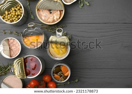 Open tin cans with different products on gray wooden table, flat lay. Space for text