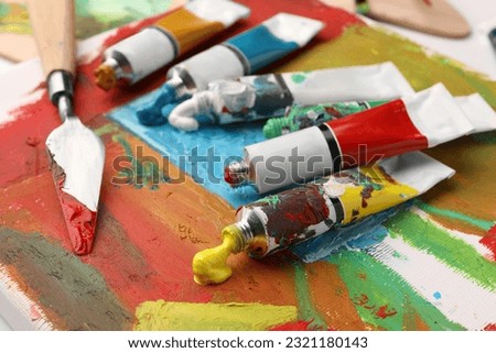 Tubes of colorful oil paints and spatula on canvas with abstract painting, closeup