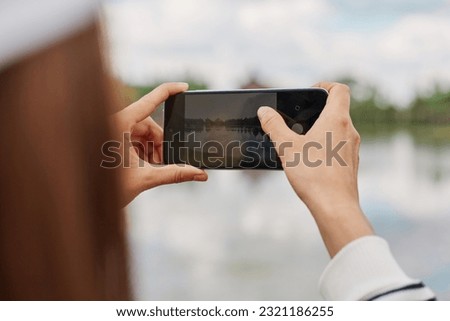 Traveler girl holding mobile phone and taking photo of beautiful nature river or lake. Atmospheric moment.