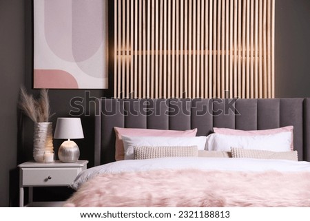 Comfortable bed with cushions, lamp and different decor on white bedside table in room. Stylish interior
