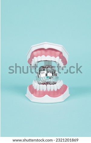  a plastic denture with a discoball in its mouth on a turquoise background. Minimal and creative color still life photography 
