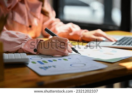 Closeup view of female economist using laptop and working with graph and statistic document on office desk