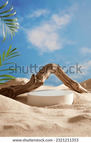 A white podium in round-shaped displayed on the sand with a big tree branch and some green tropical leaves. Blue sky background Royalty-Free Stock Photo #2321211353