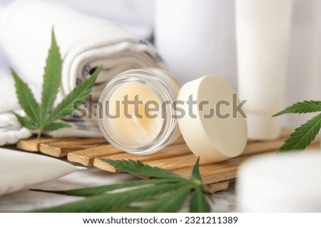 Jar with CBD lip balm and green cannabis leaves near bottles and towel in bathroom close up on a wooden tray. Organic skincare product. Alternative cosmetics
 Royalty-Free Stock Photo #2321211389