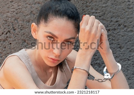 Beautiful woman handcuffed, looking into camera, gray wall.