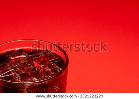 Glass full of ice cubes and a fresh cold soft drink over red background with copy space