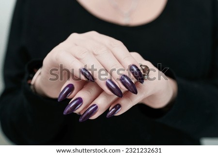 Female hands with long nails and black manicure holding a bottle of nail polish