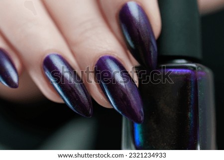 Female hands with long nails and black manicure holding a bottle of nail polish