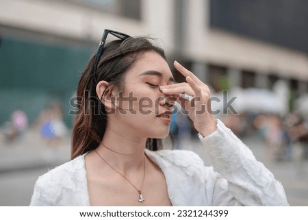 A young asian woman suffers from sinusitis or runny nose while walking around the city. Urban air pollution issues or allergens. Royalty-Free Stock Photo #2321244399
