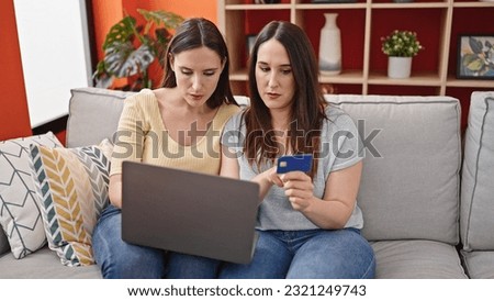 Two women sitting on sofa shopping with laptop and credit card at home
