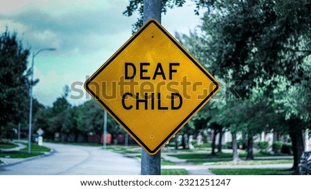 A yellow "Deaf Child" sign is posted onto a light pole on an empty neighborhood street with trees, houses, and an open street behind it