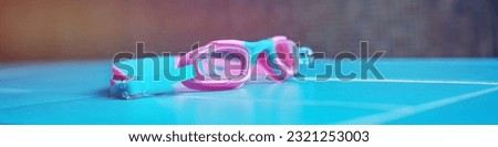 Colorful children swimming protective goggles located on tiled skirting board indoor of swim pool. Sport and recreation gear concept. Royalty-Free Stock Photo #2321253003